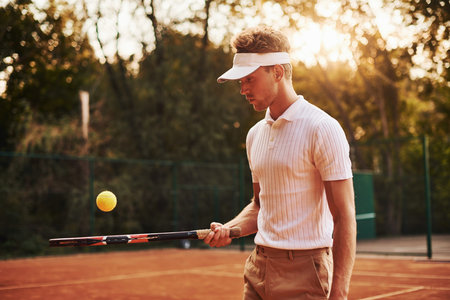 Young tennis player in sportive clothes is on the court outdoors.