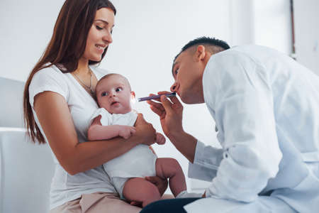 With mothers help. Young pediatrician is with little baby in the clinic at daytime.の写真素材