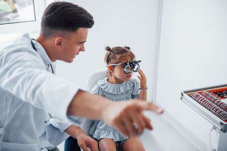 Testing vision. Young ophthalmologist is with little female visitor in the clinic.の写真素材