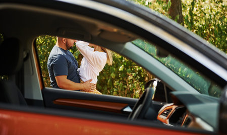Couple embracing each other in the forest near modern car.
