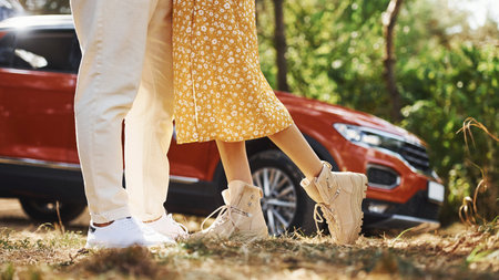 Legs of couple that embracing each other outdoors in the forest against modern vehicle.
