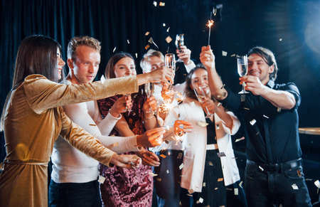 Having fun with sparklers. Group of cheerful friends celebrating new year indoors with drinks in hands.の写真素材
