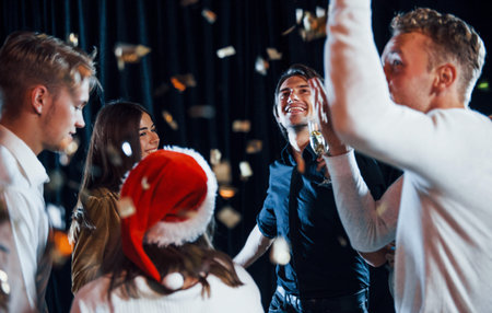 Confetti is in the air. Group of cheerful friends celebrating new year indoors with drinks in hands.