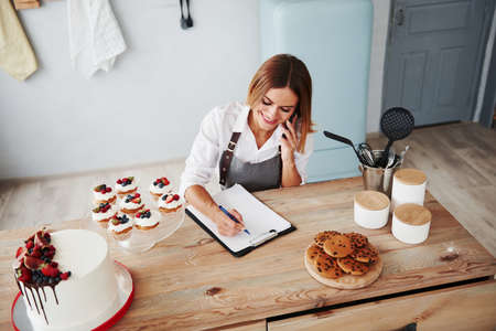 Blonde takes an order by phone. Homemade cookies and pie on the table.の写真素材