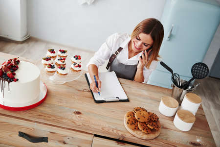 Blonde takes an order by phone. Homemade cookies and pie on the table.の写真素材