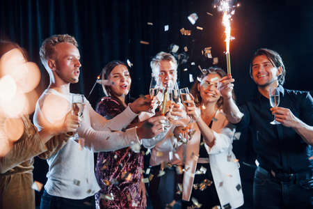 Knocking glasses. Group of cheerful friends celebrating new year indoors with drinks in hands.の写真素材