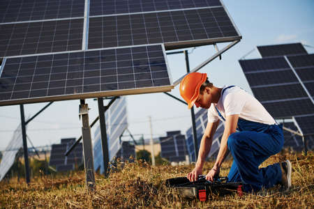 Opening case with equipment. Male worker in blue uniform outdoors with solar batteries at sunny day.の写真素材