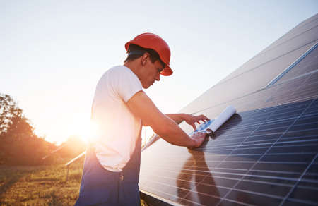 Beautiful sunlight. Male worker in blue uniform outdoors with solar batteries.の写真素材