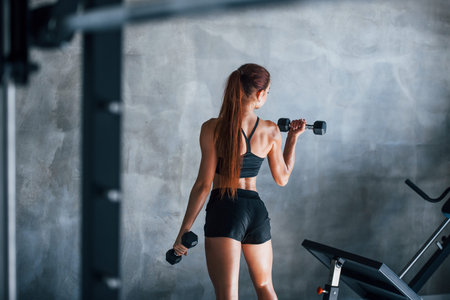 Young fitness woman with slim type of body and in black sportive clothes is in the gym.