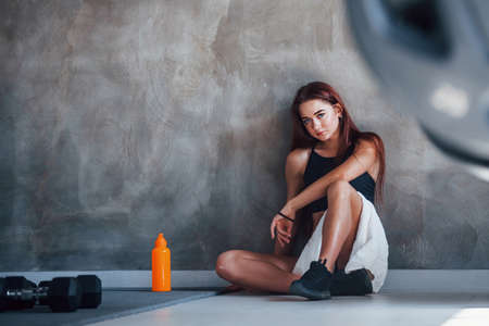 Young fitness woman sits on the floor with water in the gym.の写真素材