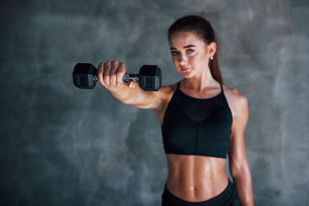 Young fitness woman is in the gym near wall with dumbbells in hands.の写真素材
