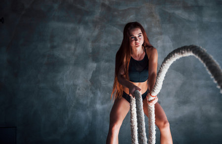 Young fitness woman with slim type of body doing exercises with knots in hands.