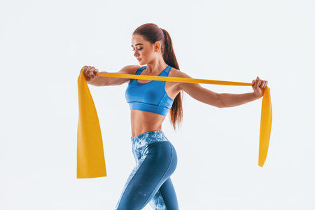 With yellow resistance band. Young woman with slim body type isolated against white background.