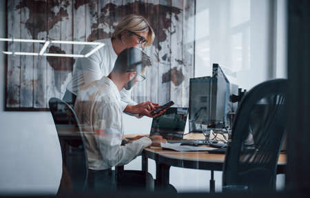 View through the glass. Two stockbrokers in formal clothes works in the office with financial market.の写真素材