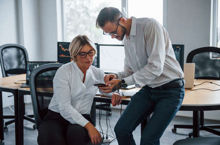 Two stockbrokers in formal clothes works in the office with financial market.