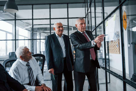 Working with stickers on glass. Aged team of elderly businessman architects have a meeting in the office.の写真素材