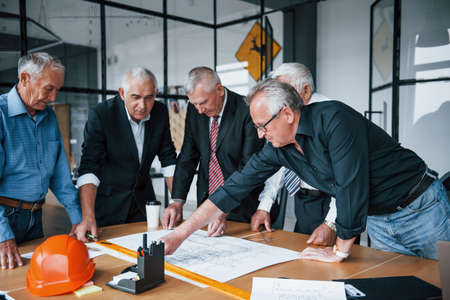 Planning construction by measuring it on paper. Aged team of elderly businessman architects have a meeting in the office.の写真素材