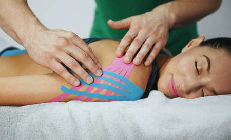 Doctor helps woman by shoulder treatment with kinesio tape.の写真素材