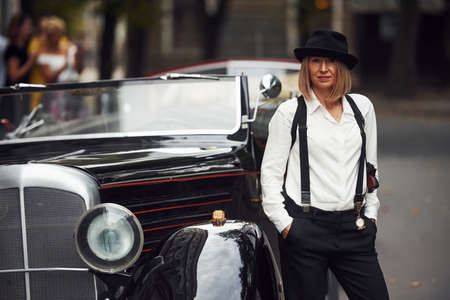 Blonde woman in hat and in black retro clothes near old vintage classic car.の写真素材