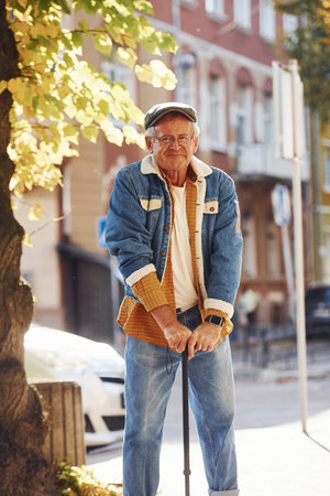 Stylish senior in fashionable clothes and in glasses have a walk in the city.