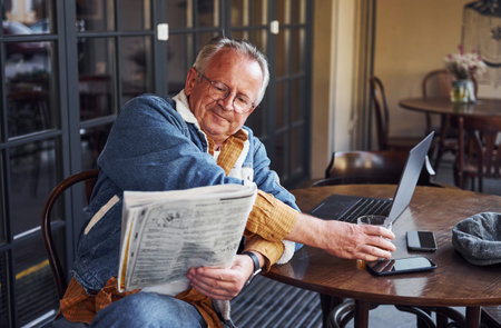Stylish senior in fashionable clothes and in glasses sits in the cafe and reads newspaper.の写真素材