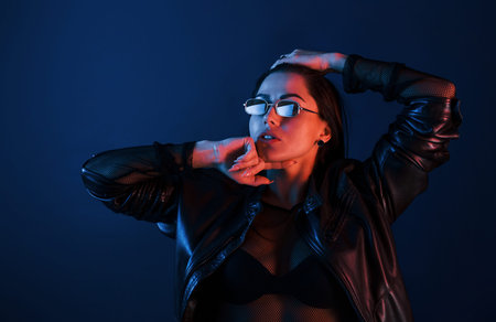Hot brunette in sunglasses posing in the studio with neon lighting.