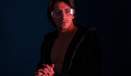 Beautiful long haired hot man in glasses is in the studio with blue neon lighting.