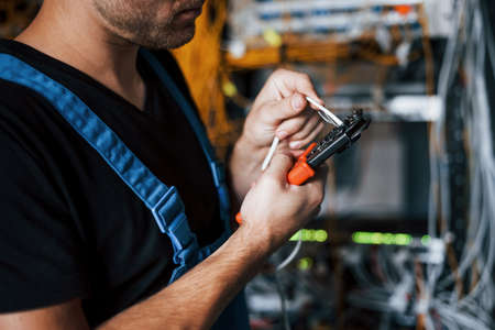 Young man in uniform works with internet equipment and wires in server room.の写真素材