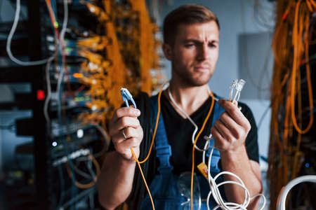 Young man in uniform feels confused and looking for a solution with internet equipment and wires in server room.の写真素材