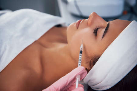 Close up view of woman that lying down in spa salon and have injection by the syringe into her face skin.の写真素材