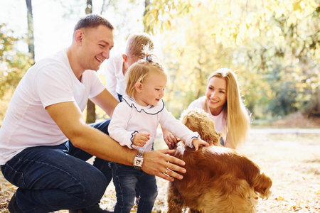 Cheerful young family with dog have a rest in an autumn park together.