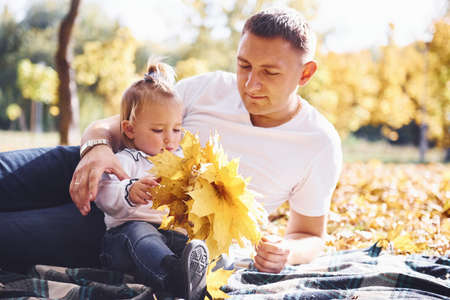 Dad with little daughter have a rest in an beautiful autumn park at sunny day.の写真素材