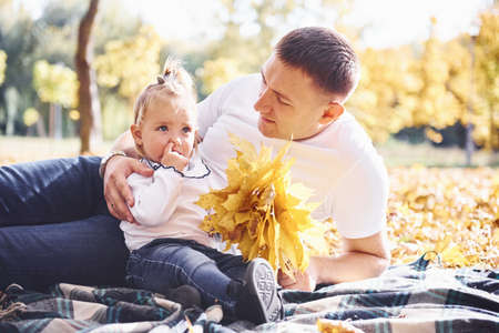 Dad with little daughter have a rest in an beautiful autumn park at sunny day.の写真素材