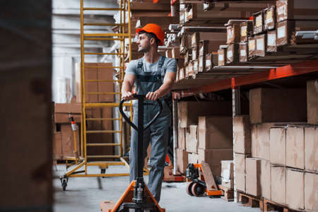 Young male worker in uniform is in the warehouse with pallet truck.の写真素材