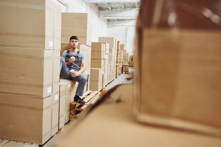 Storage worker sits and have a break. Eats sandwitch and drinks coffee.