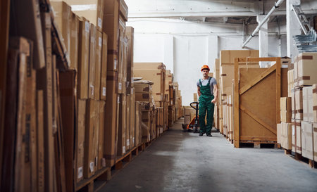 Young male worker in uniform is in the warehouse with pallet truck.