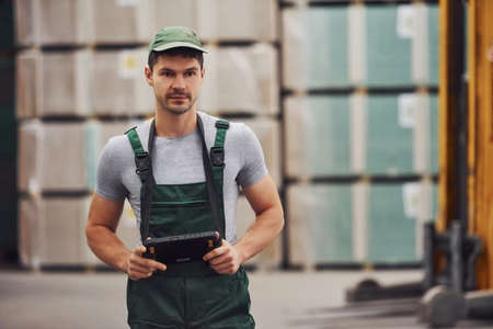 Storage worker in green colored uniform and notepad in hands checks production.の写真素材