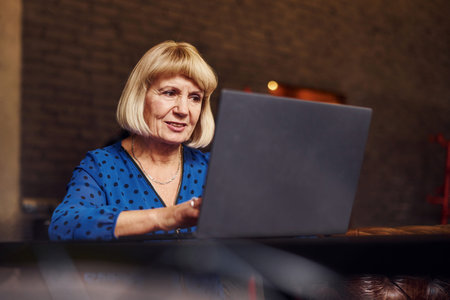 Portrait of senior woman that sits indoors in the cafe with modern laptop.