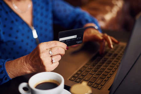 Portrait of senior woman that sits indoors in the cafe with modern laptop and credit card in hand.の写真素材