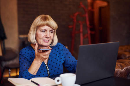Portrait of senior woman that sits indoors in the cafe with modern laptop.の写真素材