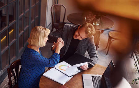Young guy in formal clothes have a business talk with old woman in cafe.の写真素材