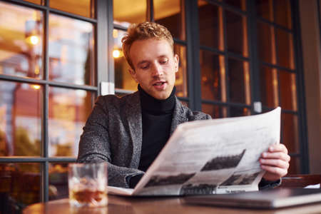 Portrait of modern young guy in formal clothes that sits in the cafe and reads newspaper.の写真素材