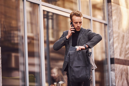 Man in elegant formal wear outside against modern building talking by the phone.