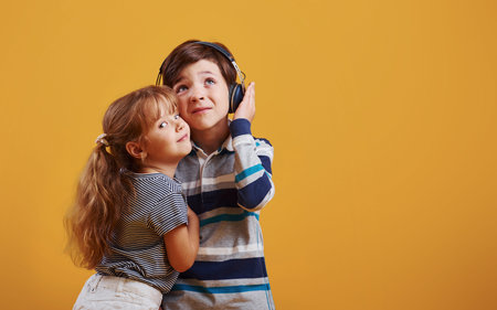 Little girl with boy stands together in the studio against yellow background.