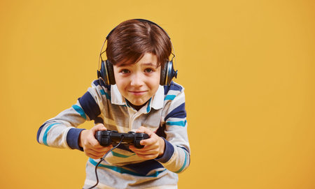 Cute little boy playing video game in the studio against yellow background.
