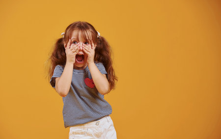 Cute little girl in casual clothes have fun in the studio against yellow background.