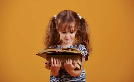 Cute little girl with book in hands in the studio against yellow background.の写真素材