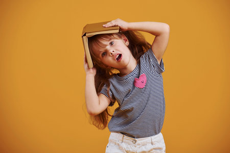 Cute little girl with book in hands in the studio against yellow background.