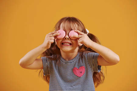 Cute little girl with sweet food in the studio against yellow background.の写真素材
