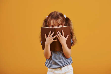 Cute little girl with book in hands in the studio against yellow background.の写真素材